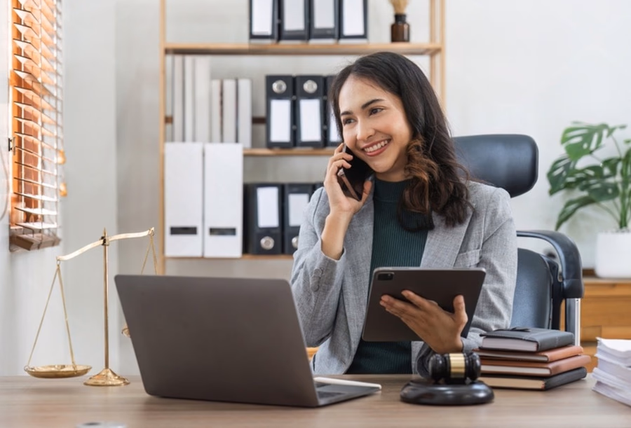 Female lawyer working in office on phone with laptop and legal documents.